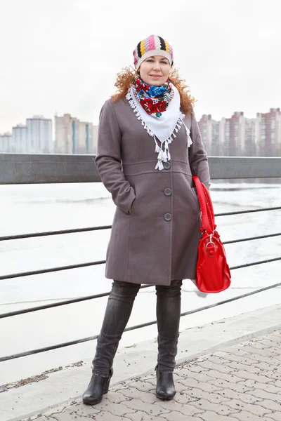 Porträt einer glücklichen jungen Kaukasierin mit roter Tasche, die auf einem Damm steht. — Stockfoto
