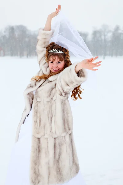 Mooie Kaukasische Russische bruid in witte jurk en in bontjas dansen op besneeuwde veld in winterseizoen, Rusland — Stockfoto