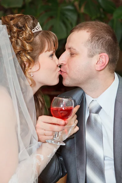 Nieuw wo paar met huwelijksgeschenken Bruidsjapon en donker pak: bruid en bruidegom roosteren met wijn en genieten er van huwelijksdag met een kus — Stockfoto