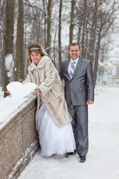 Unga bröllop kaukasiska ryska par hålla en snöig hjärta på bron. vintersäsongen i Ryssland — Stockfoto