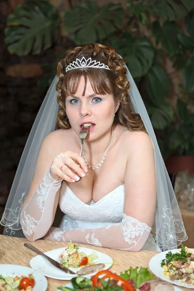 Happy bride sitting at a table of a luxury restaurant and biting fork — Stock Photo, Image