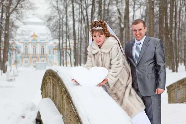 Młody wesele kaukaski kilka rosyjskich gospodarstwa snowy serce na most. sezon zimowy w Rosji — Zdjęcie stockowe