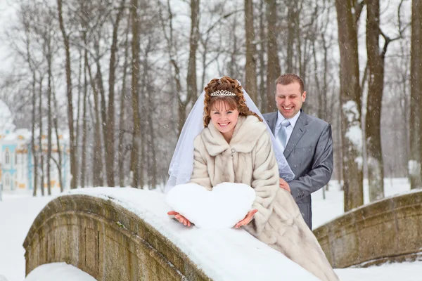 Boda joven pareja rusa caucásica sosteniendo un corazón cubierto de nieve en el puente. Temporada de invierno en Rusia —  Fotos de Stock