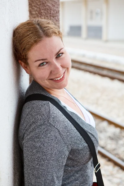 Szczęśliwa młoda kobieta kaukaski stojący w pobliżu ściany i uśmiechając się — Zdjęcie stockowe