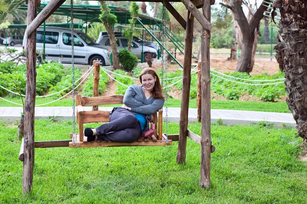 年轻女子坐在沿花园秋千和微笑 — 图库照片