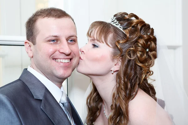 Unga kaukasiska ryska bröllopsparet. bruden kysser brudgummen i kinden — Stockfoto