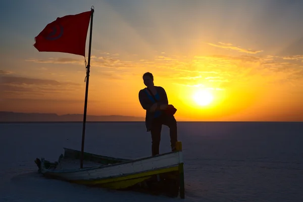 stock image Woman silhouette with flag of Tunisia against sunrise lights. Broken boat on salina area