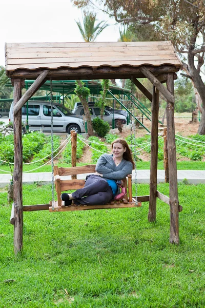 Mujer joven sentada en el jardín balancéate y sonríe — Foto de Stock