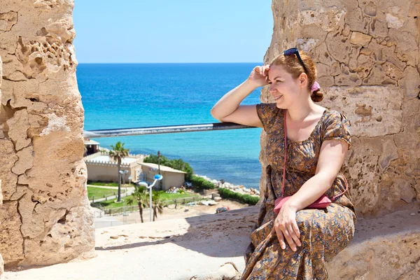 Ung kvinna med solglasögon sitter på väggen av gamla fästning och ler — Stockfoto