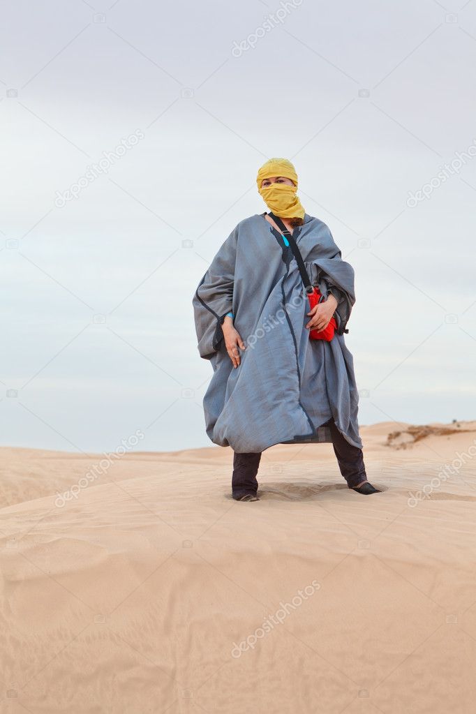 Woman in bedouin clothes standing on dune in desert