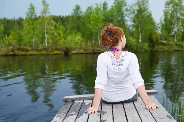 Mujer joven girando hacia atrás sentado en tablas de madera en el borde del estanque — Foto de Stock