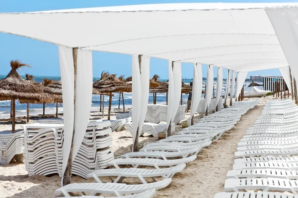 Białe plastikowe leżaki w piaszczystej plaży pod dużym parasolem — Zdjęcie stockowe