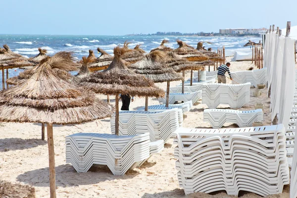 Białe plastikowe leżaki w piaszczystej plaży pod dużym parasolem — Zdjęcie stockowe