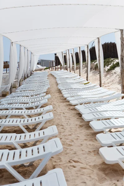 Λευκό πλαστικό ξαπλώστρες στην άμμο κάτω από μεγάλες ομπρέλες — Φωτογραφία Αρχείου