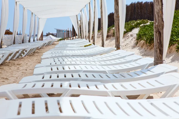 Weiße Plastikliegen im Sandstrand unter großem Sonnenschirm — Stockfoto