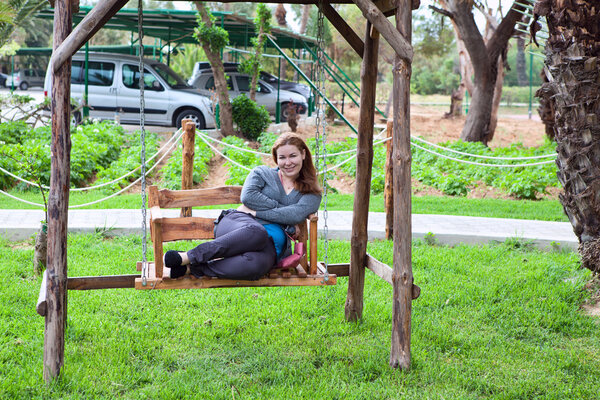 Young woman sitting on the garden swing along and smile
