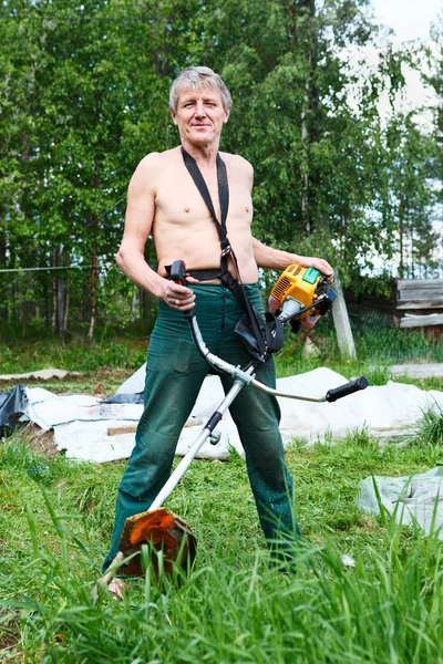 Oudere blanke man een grasmaaier met chopper trimeer gras maaien. — Stockfoto