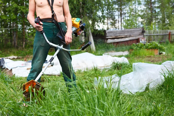 Onherkenbaar persoon een grasmaaier met chopper trimeer maaien gras. focus op trimeer — Stockfoto