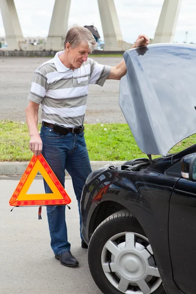 Dojrzały mężczyzna z trójkąta awaryjnych stoi przed pojazdów lądowych — Zdjęcie stockowe