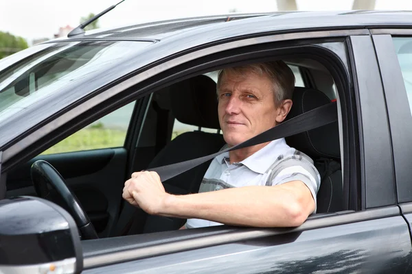 Smiling Caucasian senior male fastens safety belt sitting in car on driver seat — Stock Photo, Image