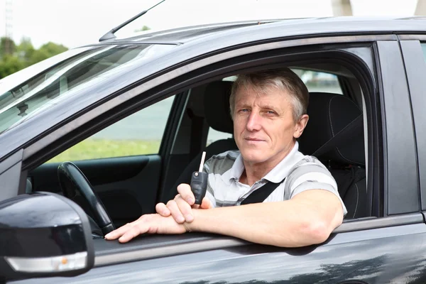 Feliz macho mayor con llave de encendido sentado en el coche en el asiento del conductor y sonriendo —  Fotos de Stock