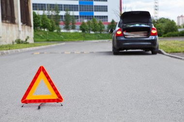 Triangle warning sign on road foreground and broken car with blinker lights on road wayside clipart