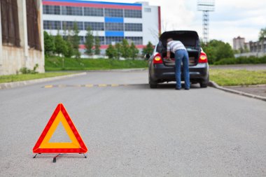 Triangle warning sign on road foreground and driver in car luggage rack clipart