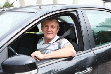 Fastened smiling Caucasian senior man sitting in car on driver seat clipart