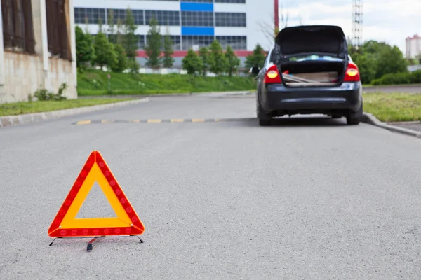 Triangle warning sign on road foreground and broken car with blinker lights on road wayside — Stock Photo, Image