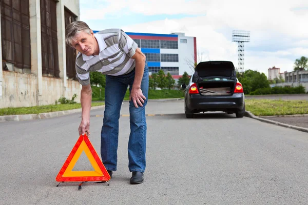 Homem maduro define triângulo aviso sinal na estrada e vai de carro com luzes pisca-pisca no esquecimento — Fotografia de Stock