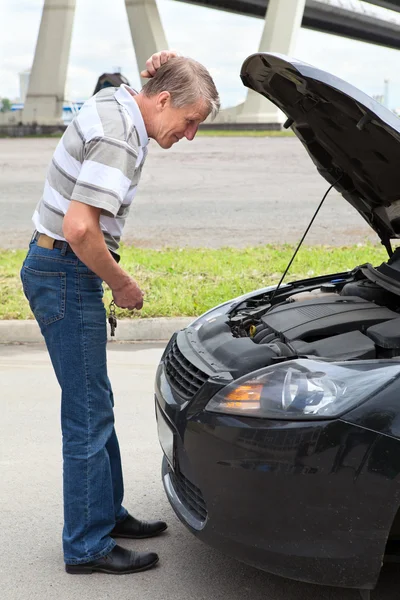 Confused mature driver standing in front of car with opened engine compartment hood — Stock Photo, Image