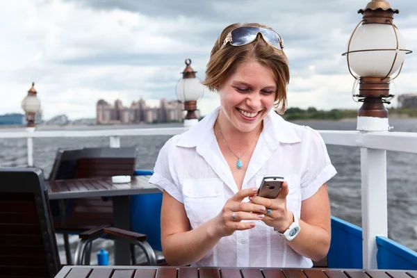 Mujer joven en la cafetería del barco escribiendo un mensaje en el teléfono móvil —  Fotos de Stock