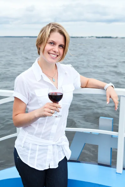 Sorrindo jovem mulher de pé na proa do navio e segurando copo de vinho tinto na mão — Fotografia de Stock