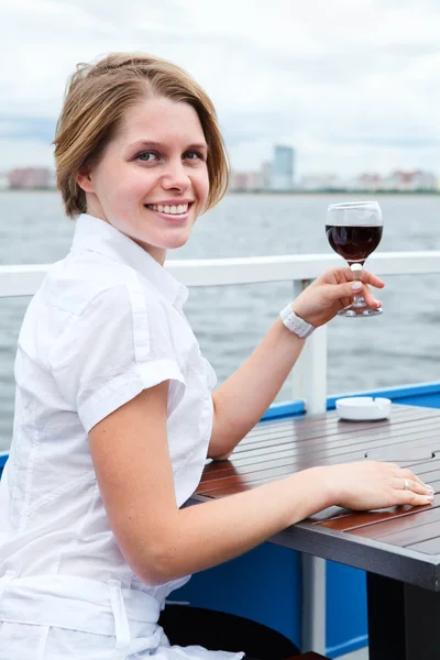 Дивлячись ззаду жінка тримає червоний келих вина і сидить за столом кафе — стокове фото