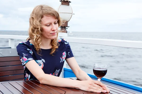 Masada oturmuş Şarap kadehi ile içinde dalgın kadın — Stok fotoğraf