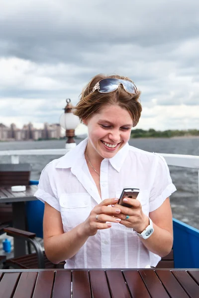 Mujer feliz en la cafetería del barco escribiendo un mensaje en el teléfono móvil —  Fotos de Stock
