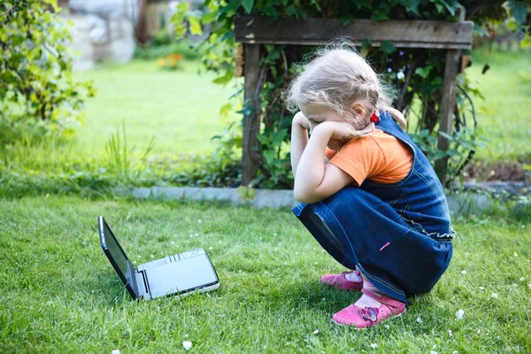 Маленька зацікавлена дівчинка дивиться DVD фільми на пристрої в зеленому газоні — стокове фото