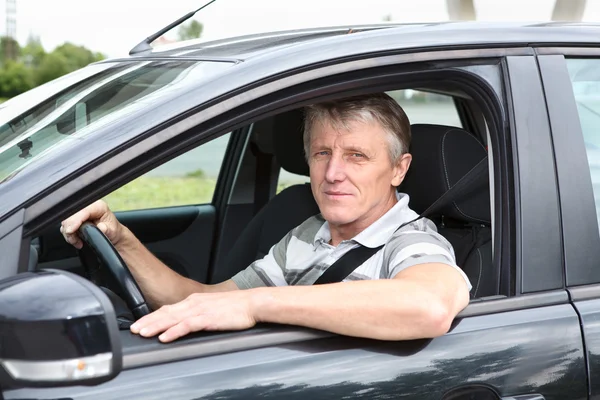 Feliz hombre mayor sentado en el coche en el asiento del conductor y sonriendo —  Fotos de Stock