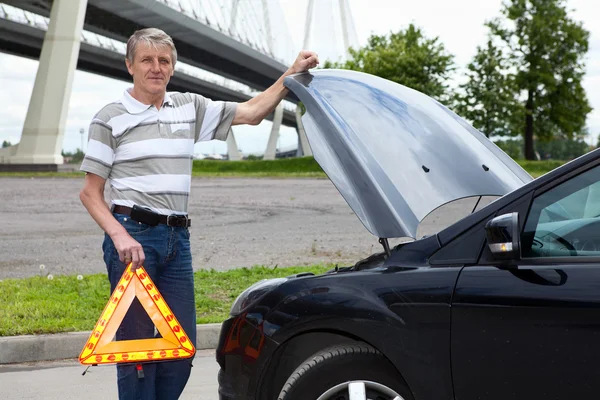 Mature man holding emergency triangle and opened car hood — Stock Photo, Image