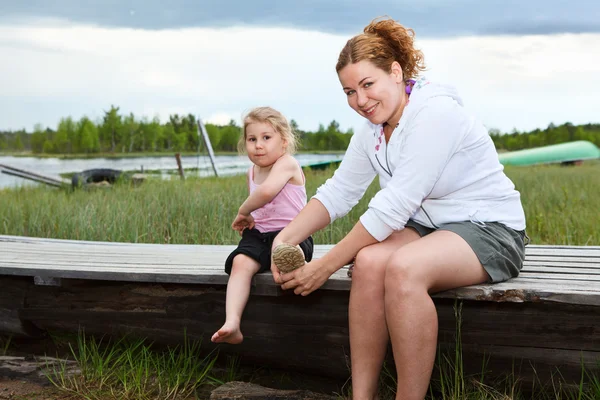 Mutter hilft kleiner Tochter, Stiefel auf Fluss zu tragen — Stockfoto