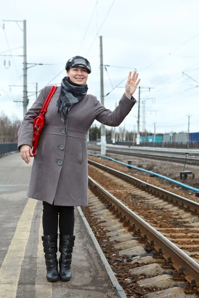 Vrouw in jas en cap met rode zak wave goodbye staande op treinstation — Stockfoto
