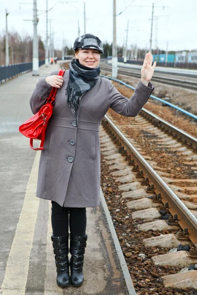 Woman in coat and cap wave goodbye standing on train station — Stock Photo, Image