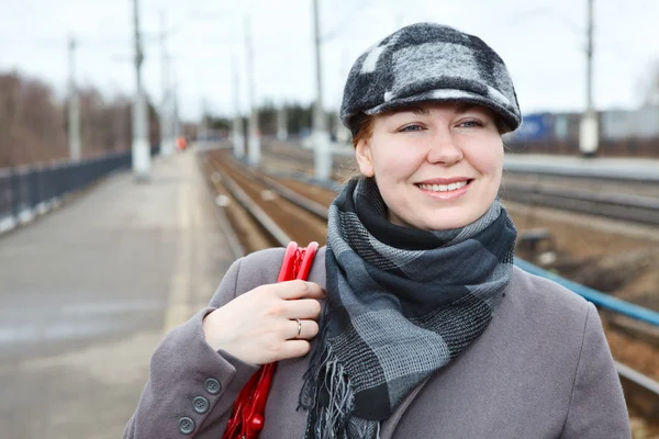 Portrait of happy smiling woman in cap standing on railway station — Stock Photo, Image