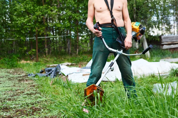 Un hombre irreconocible una cortadora de césped con cortadora de helicópteros cortando hierba. Enfoque en trimer —  Fotos de Stock