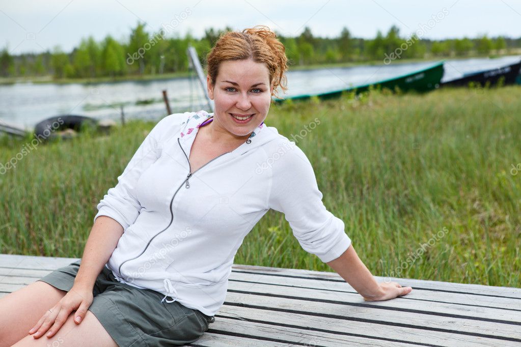 Happy smiling woman sitting on wooden boards on river edge. Copyspace