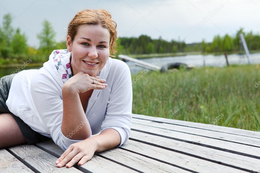 Happy smiling woman laying on wooden boards on river edge. Copyspace