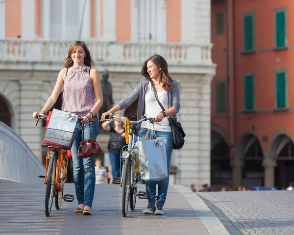 Dos hermosas mujeres caminando por la ciudad con bicicletas y bolsas — Foto de Stock