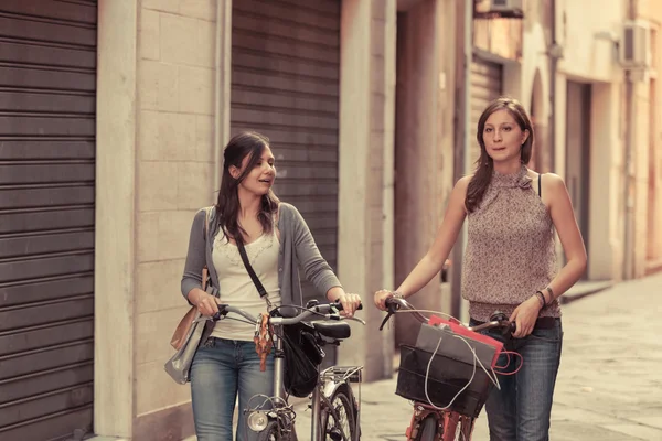 Две красивые женщины, гуляющие по городу с велосипедами и сумками — стоковое фото