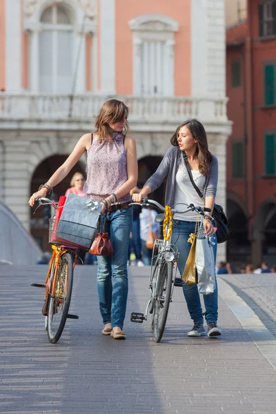 Duas mulheres bonitas andando na cidade com bicicletas e sacos — Fotografia de Stock