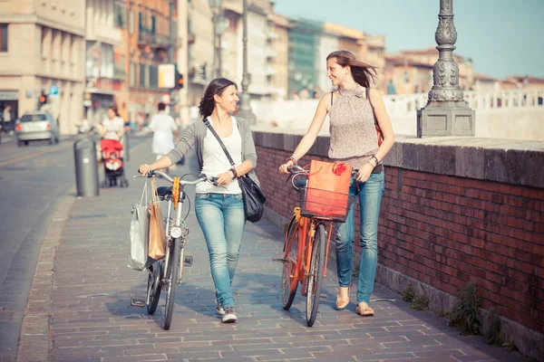 Bisiklet ve çantaları ile şehir içinde yürüyen iki güzel kadın — Stok fotoğraf